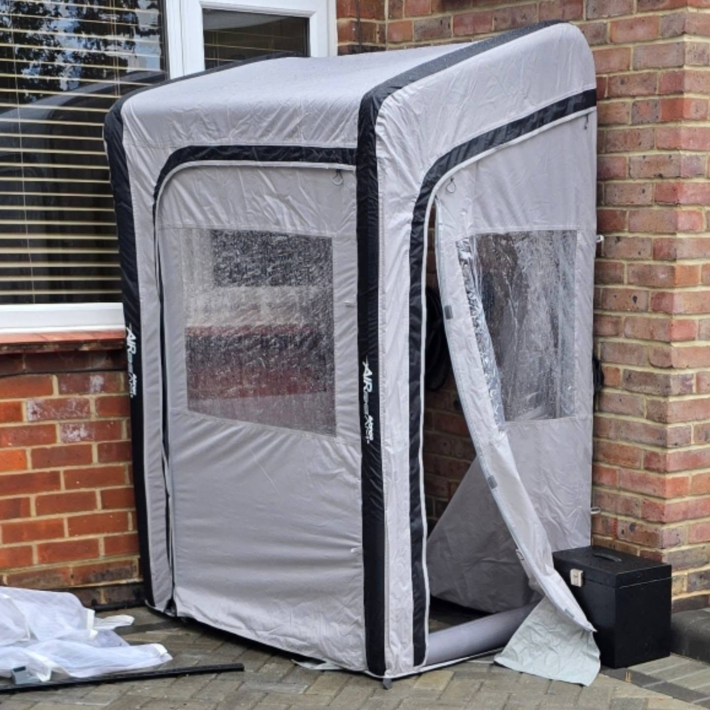 A pop-up rain shelter set up on a driveway beside a house